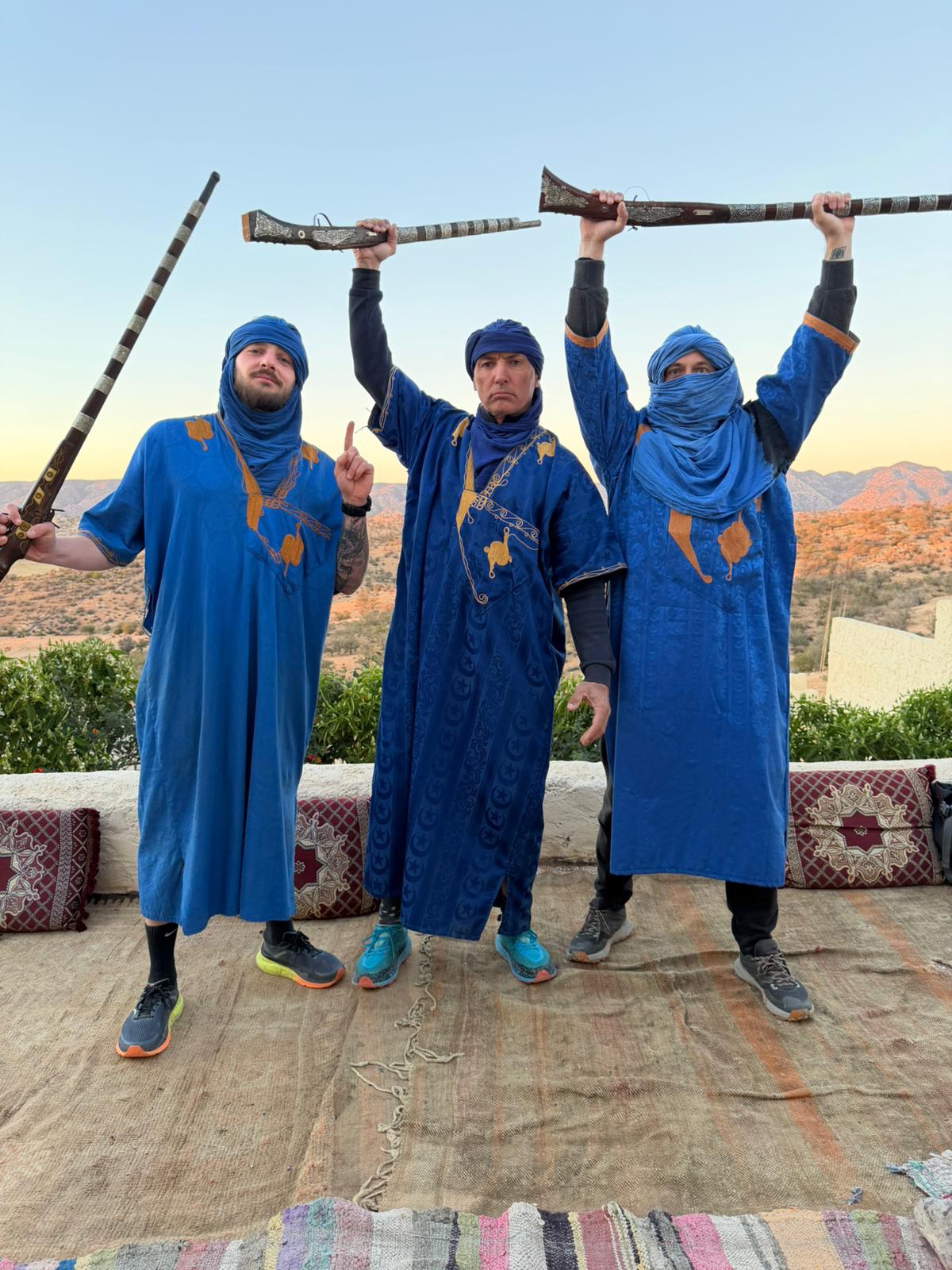Trois voyageurs en tenue traditionnelle bleue levant des fusils décorés