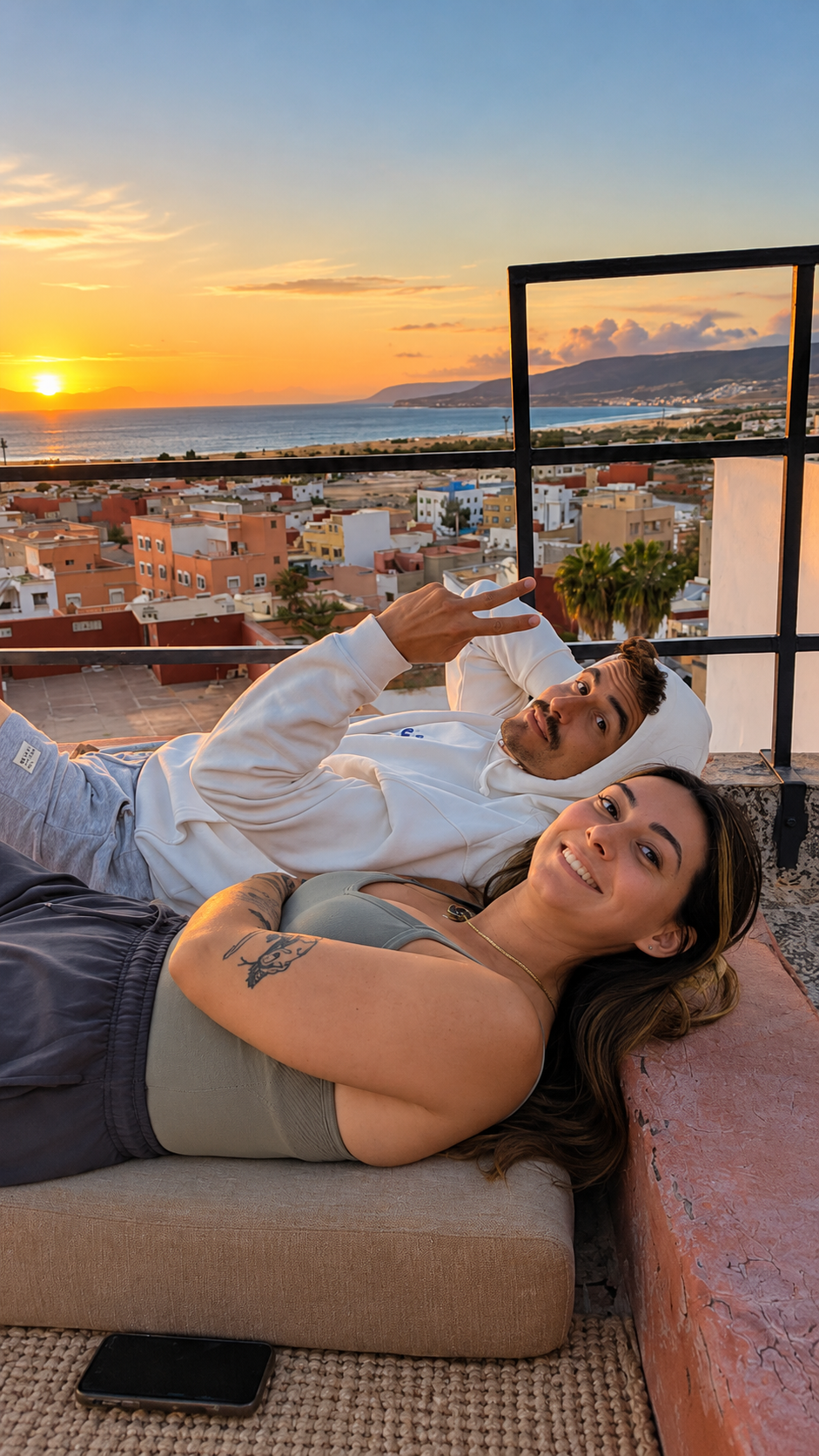 Couple allongé sur un rooftop à Taghazout au coucher du soleil, vue sur l'océan et le village