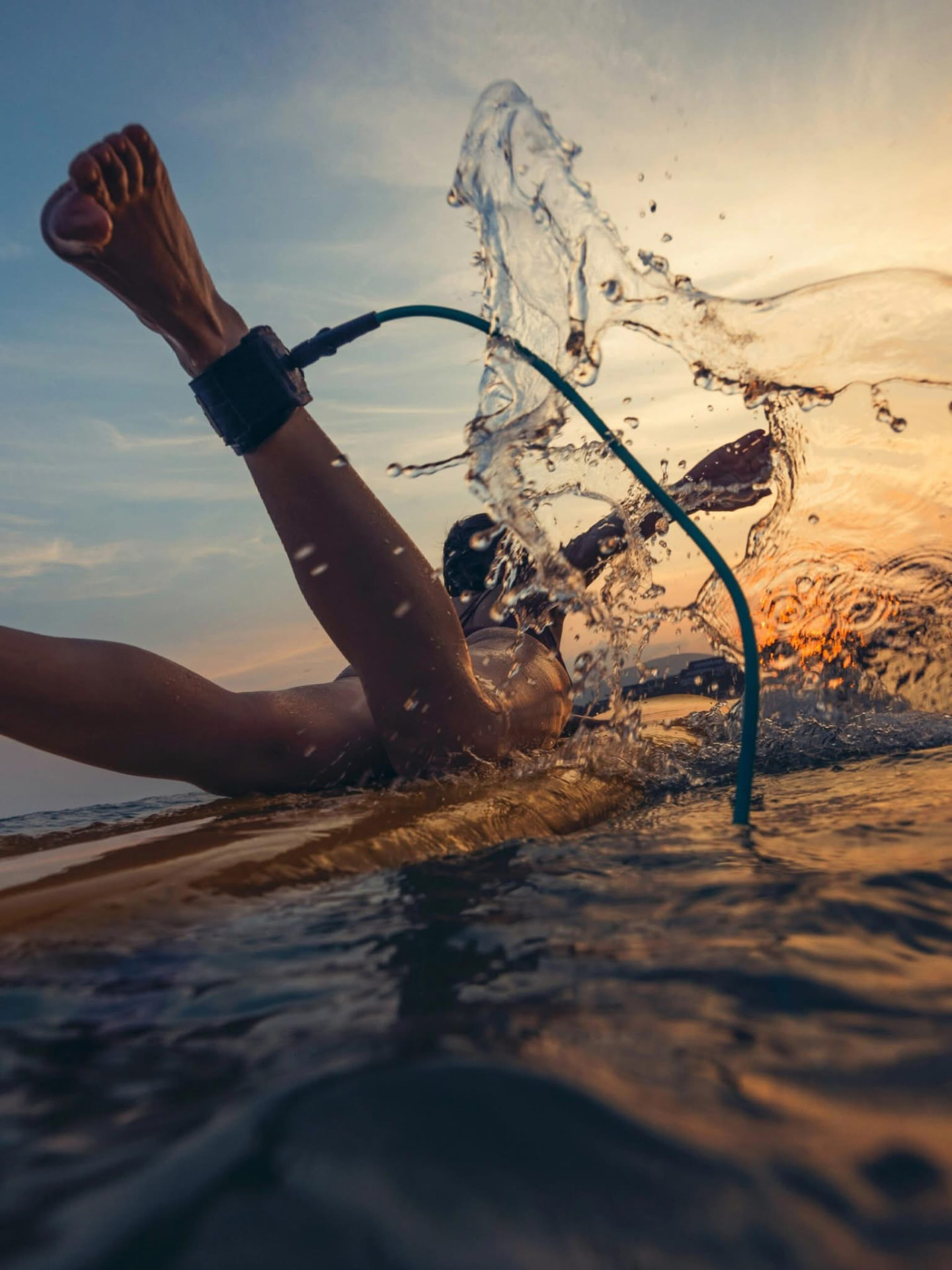 Surfeur pagayant sur sa planche au coucher du soleil, éclaboussures d'eau dorée