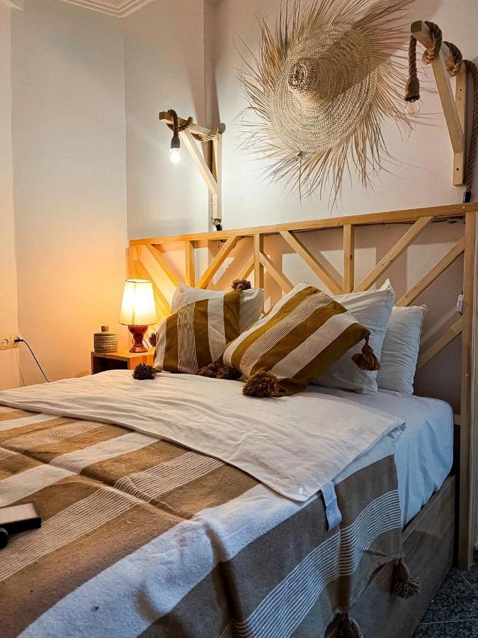 Chambre privée WAVESKY à Taghazout : lit double avec tête de lit en bois, coussins marocains et lampe chaude