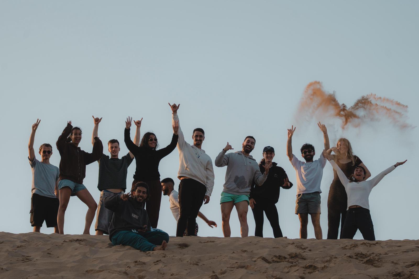 Groupe de surfeurs célébrant sur une dune avec de la fumée orange