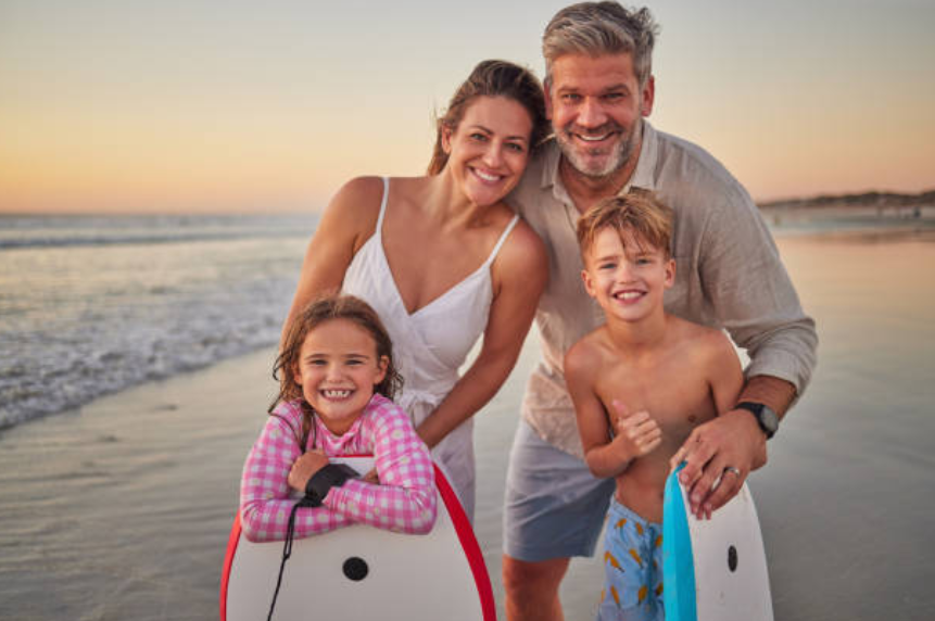 Famille souriante avec des bodyboards sur la plage au coucher du soleil
