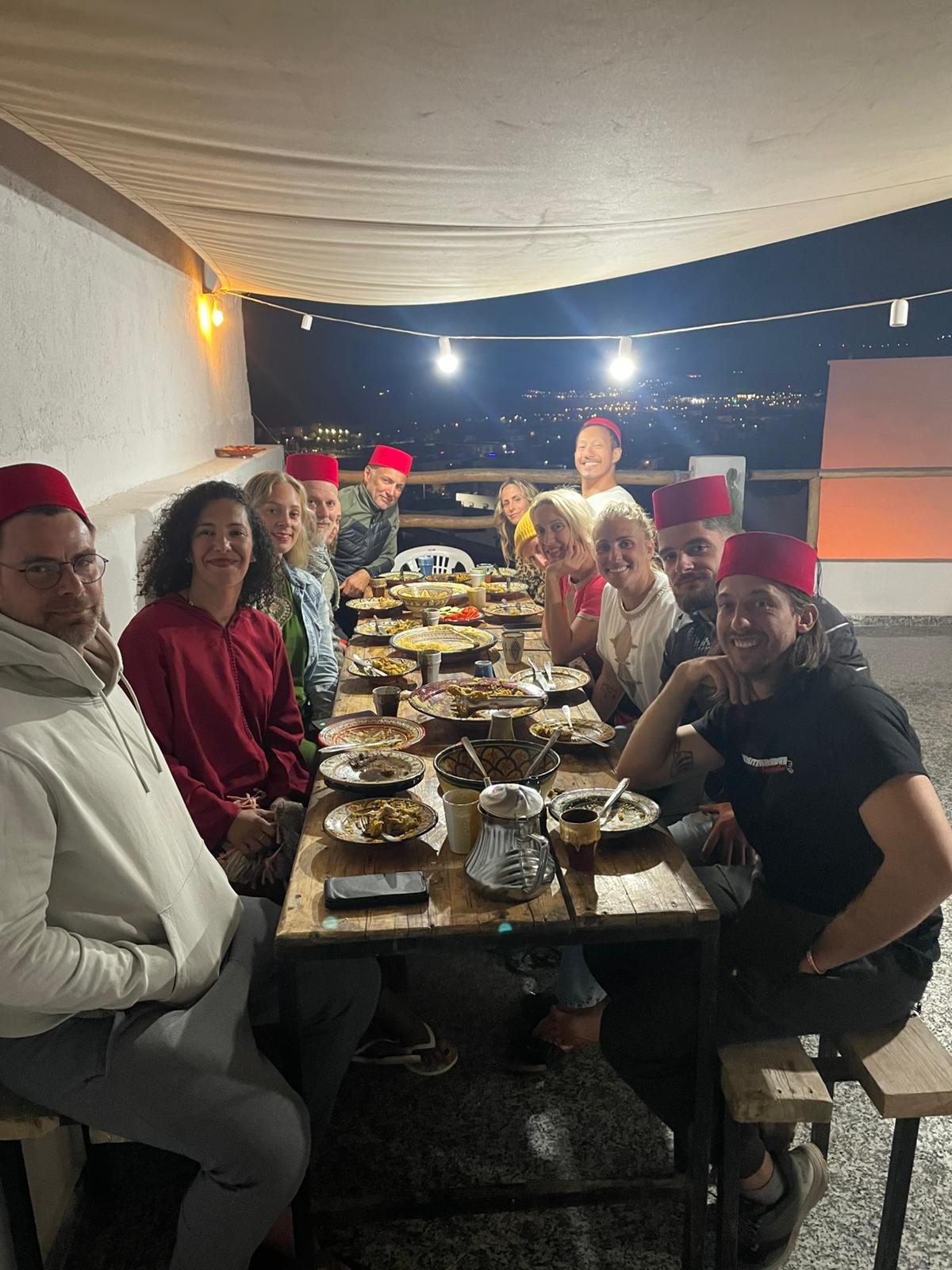 Grande tablée sur le rooftop la nuit, chapeaux rouges et plats marocains
